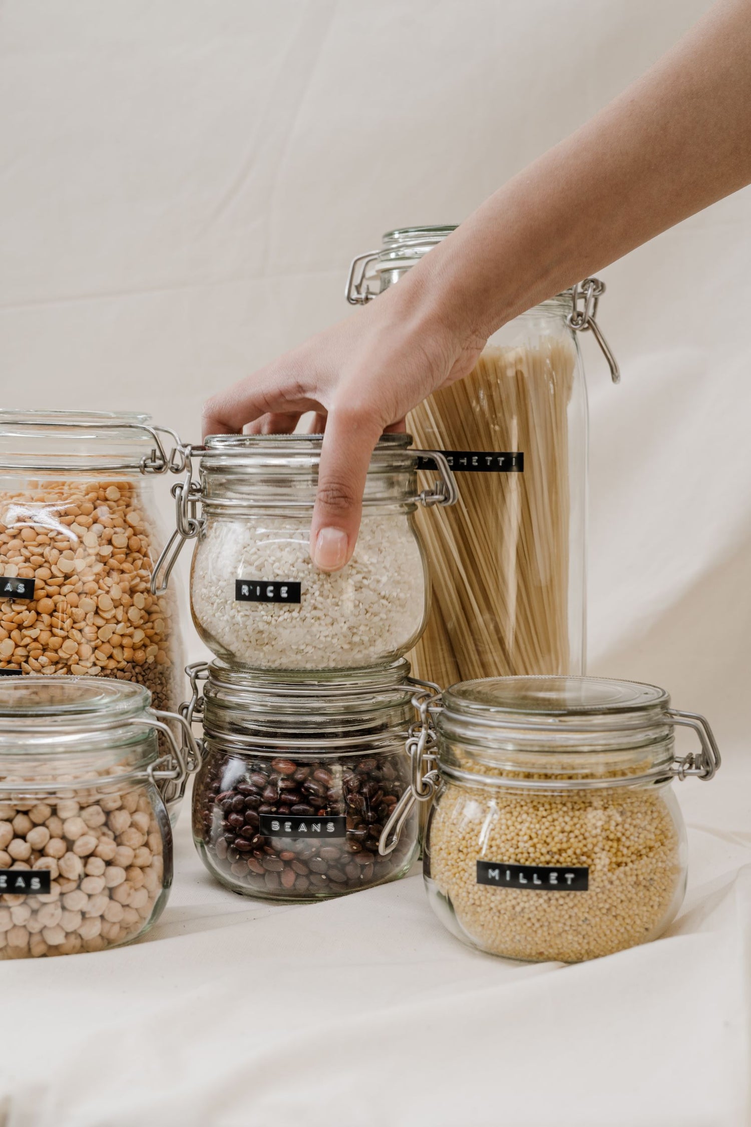 Hand reaching for a glass jar of rice among jars of beans, millet, and pasta at Bulk Food Warehouse's bring your own container section in Aldershot, serving Burlington, Hamilton, and Halton communities.